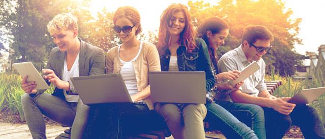a group of students sitting on a bench with laptops.