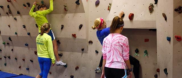 four girls climbing a rock wall inside Ganfield Gymnasium